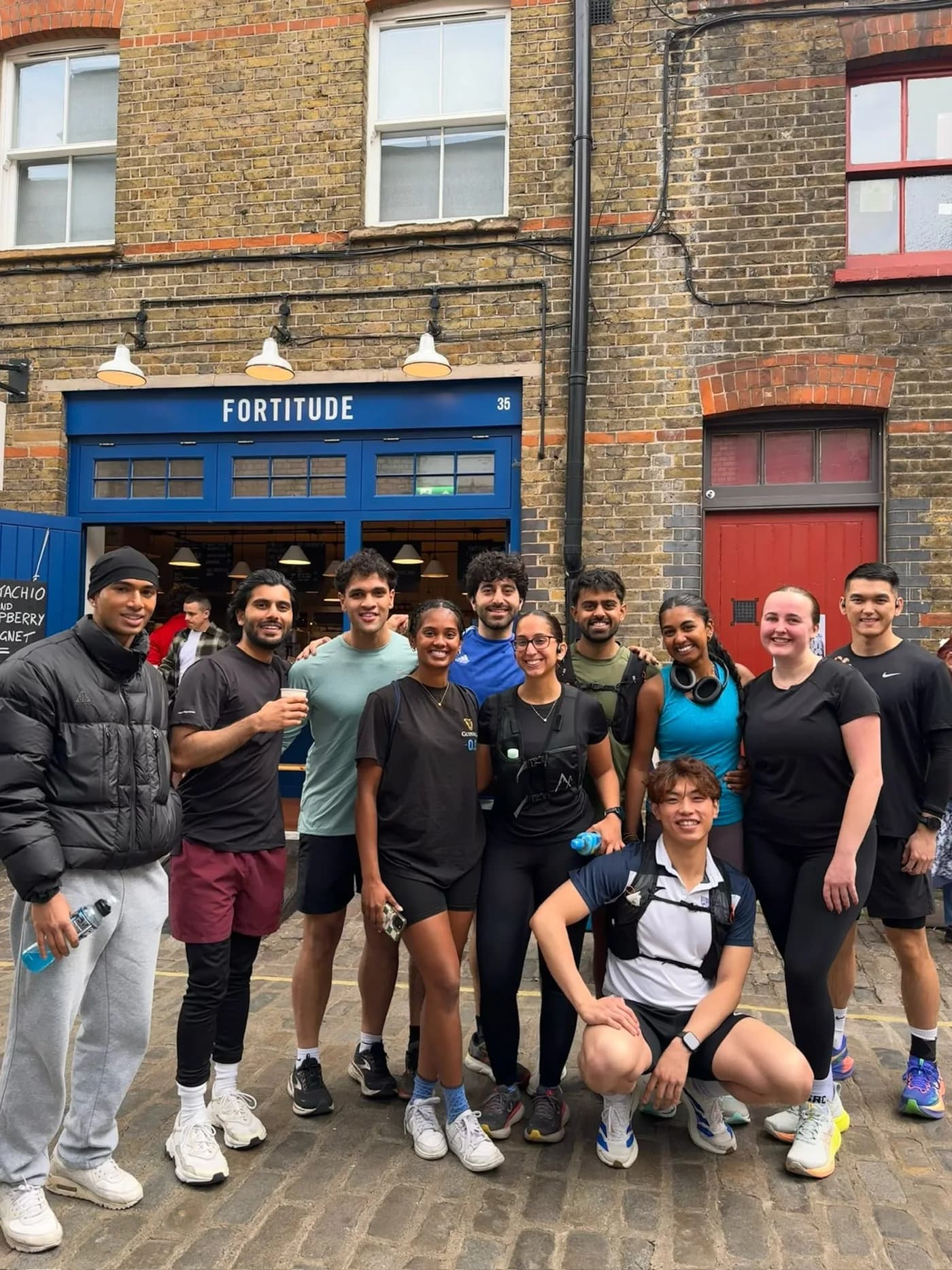 A group in sportswear smiling together outside a café on a cobbled street